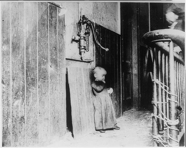 Jacob Riis, ca. 1888 — a baby in a tenement hallway